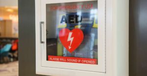 A display case holding an automated external defibrillator reads, "FOR EMERGENCY USE - AED - ALARM WILL SOUND IF OPENED."