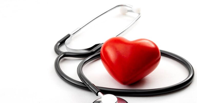 A stethoscope and a red heart against a white hospital background. The stethoscope has its PVC tubing around the heart.