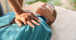 A close-up of a person's hands performing CPR on a medical training manikin that's wearing a blue vest.