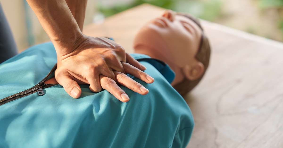 A close-up of a person's hands performing CPR on a medical training manikin that's wearing a blue vest.