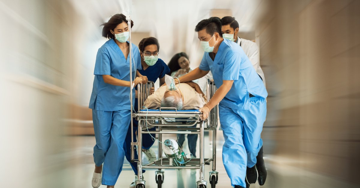 Doctors, nurses, and paramedics transport a patient on a gurney through a hospital corridor wearing protective masks.