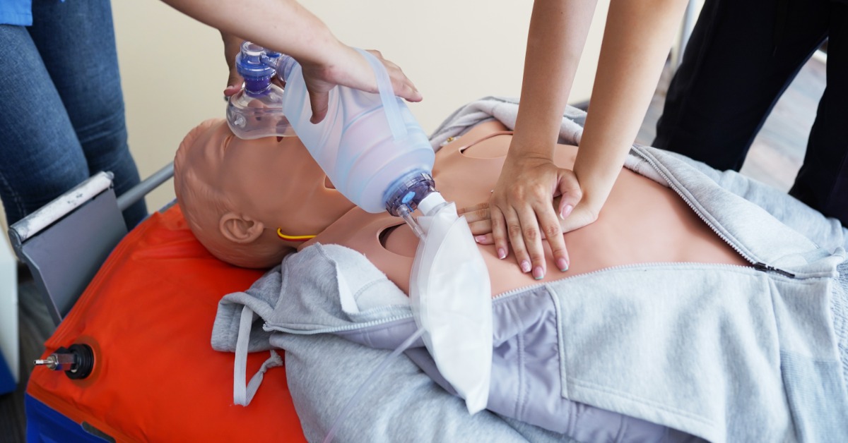 Healthcare trainees perform CPR and bag-valve-mask ventilation on a medical manikin during hands-on emergency training.