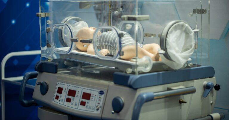 A neonatal training manikin inside a medical incubator used for pediatric emergency simulations during PALS training.
