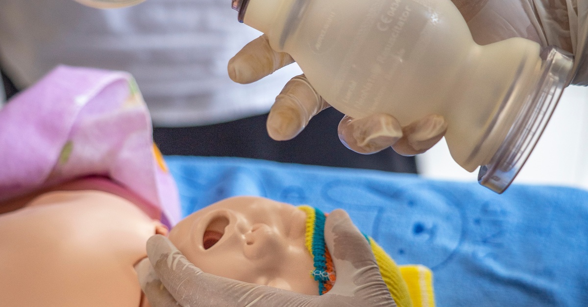 A healthcare provider performs neonatal resuscitation on an infant mannequin using a bag valve mask during NRP training.