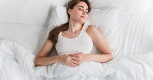A young woman sleeping peacefully in a white bed with white pillows and blankets, showing the benefits of quality rest.