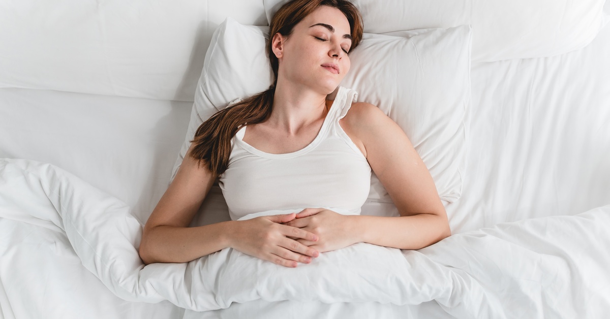A young woman sleeping peacefully in a white bed with white pillows and blankets, showing the benefits of quality rest.