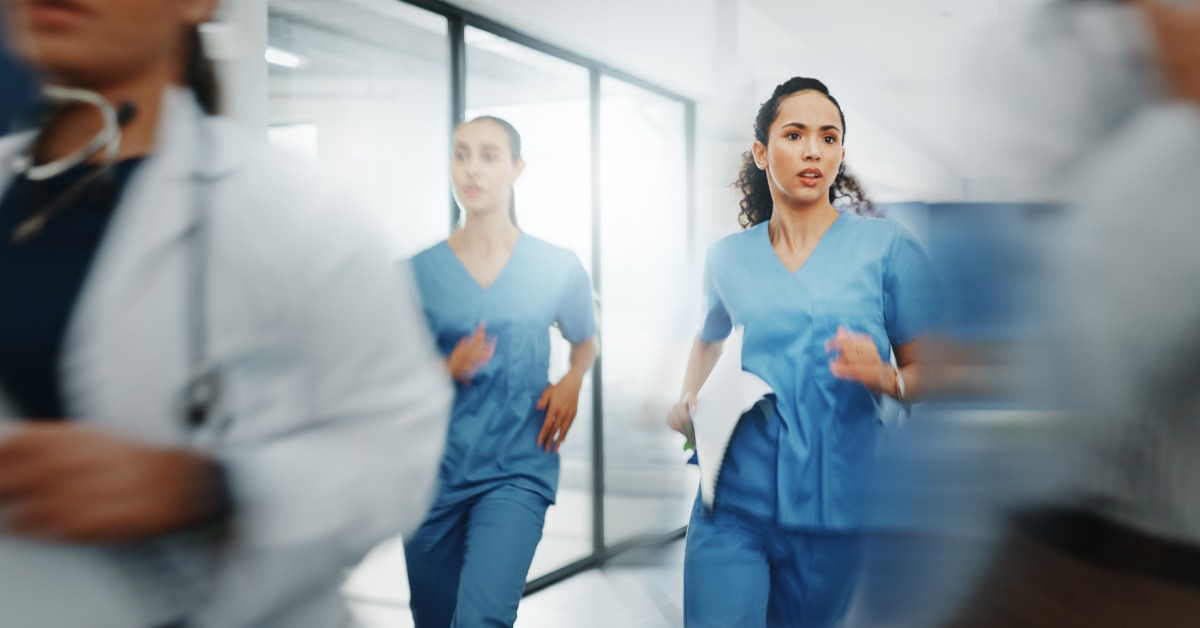 A trauma nurse in blue scrubs runs urgently down a hospital corridor alongside medical colleagues during an emergency