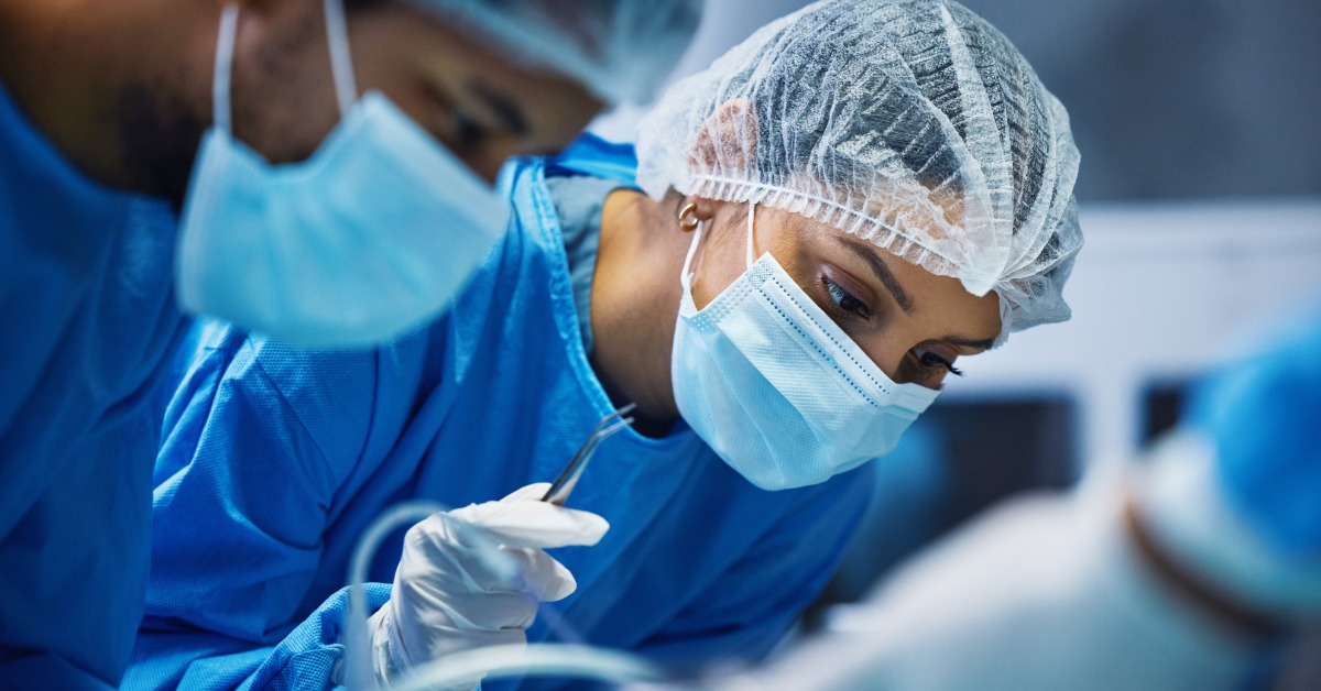 A focused trauma nurse in surgical scrubs and a face mask performs a procedure alongside a colleague in the operating room.