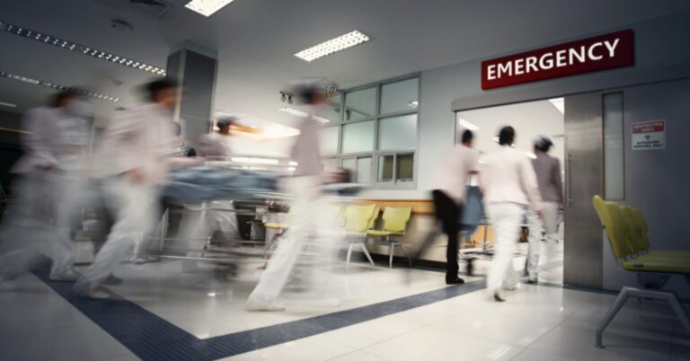 Nurses and medical staff rush a patient on a gurney through a busy hospital emergency department corridor.