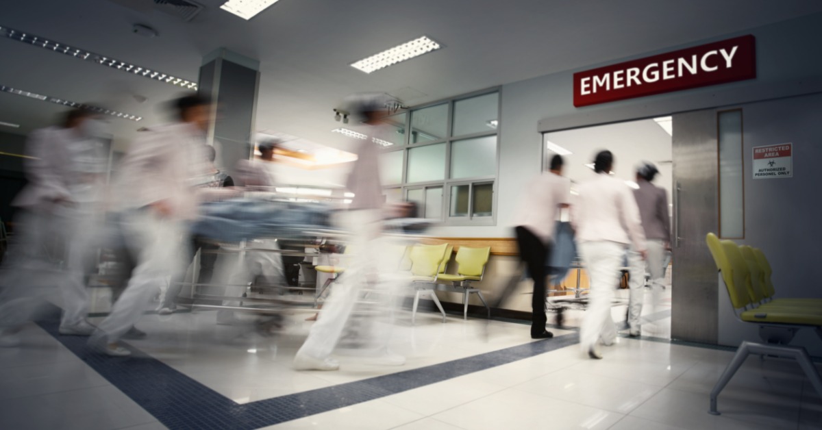 Nurses and medical staff rush a patient on a gurney through a busy hospital emergency department corridor.