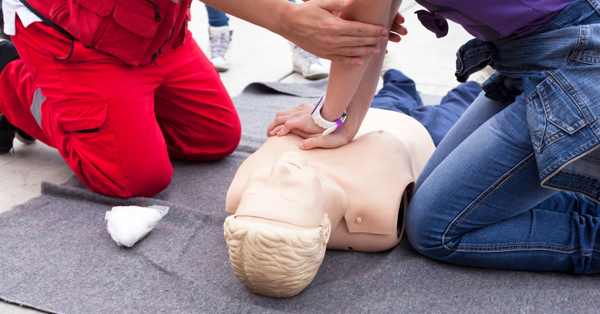 An instructor guides a student through CPR chest compressions on a training mannequin during a hands on first aid class.