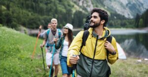 A group of hikers with backpacks and trekking poles walk near a mountain lake, prepared for a remote wilderness trip
