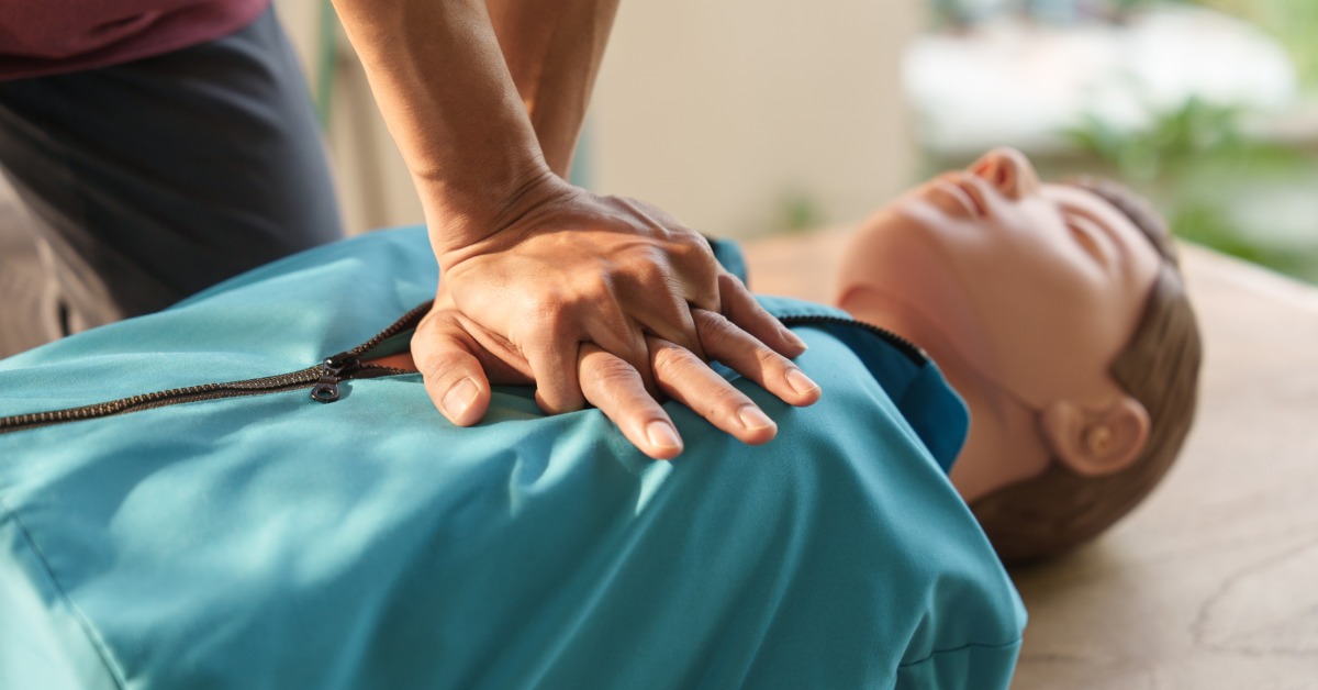 A close-up of a person's hands clenched into a fist to perform CPR on a training dummy with a blue jacket.
