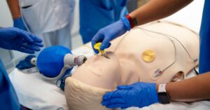A close-up of a medical training mannequin on a table as healthcare students practice endotracheal intubation.