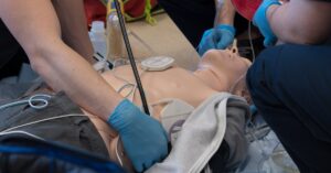 Healthcare providers practice airway management and defibrillator pad placement on a training manikin during an ACLS class.